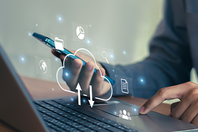 Cloud-Symbol vor Nahaufnahme von Händen die an einem Laptop ein Smartphone halten